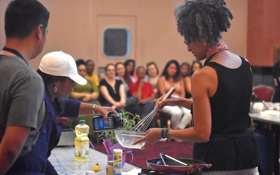 Celebrity chef Carla Hall gets some help from one of the cooks she's tutoring during a demonstration Wednesday, Aug. 23, 2017 at La Bella Vista Club at Aviano Air Base, Italy.