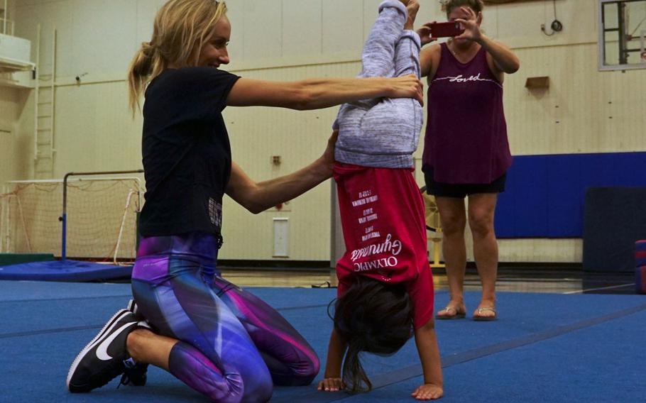 Nastia Liukin, all-around women's gymnastics champion and three-time silver medalist at the 2008 Summer Olympics, helps a child perform a handstand during a youth gymnastics clinic at Yokota Air Base, Japan, Thursday, Aug. 30, 2017.