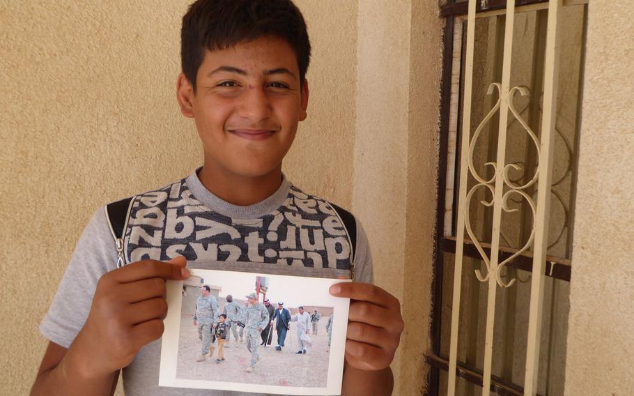 Ismail, 16, son of Jeddalah's slain sheikh, Dr. Mohammed Ismail, pictured here on Friday, September 8, 2017, holds an undated photo from about 2008 where he is pictured walking with a U.S. Army colonel. His father is seen walking with crutches behind the Americans. He'd had his legs amputated in a roadside bomb attack earlier that year.