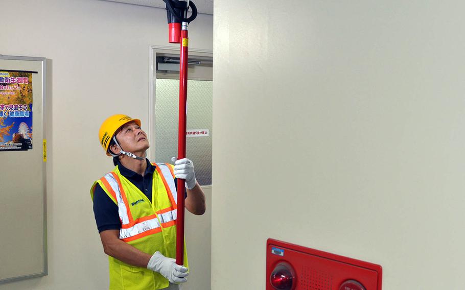 A public works employee tests a smoke detector inside an office at Yokosuka Naval Base, Japan, Friday, Oct. 13, 2017.