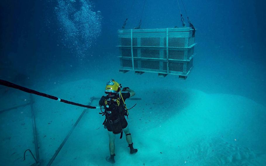 A Navy diver guides a salvage basket during an underwater recovery operation searching for World War II remains off the coast of Koror, Palau, Jan. 30, 2018.