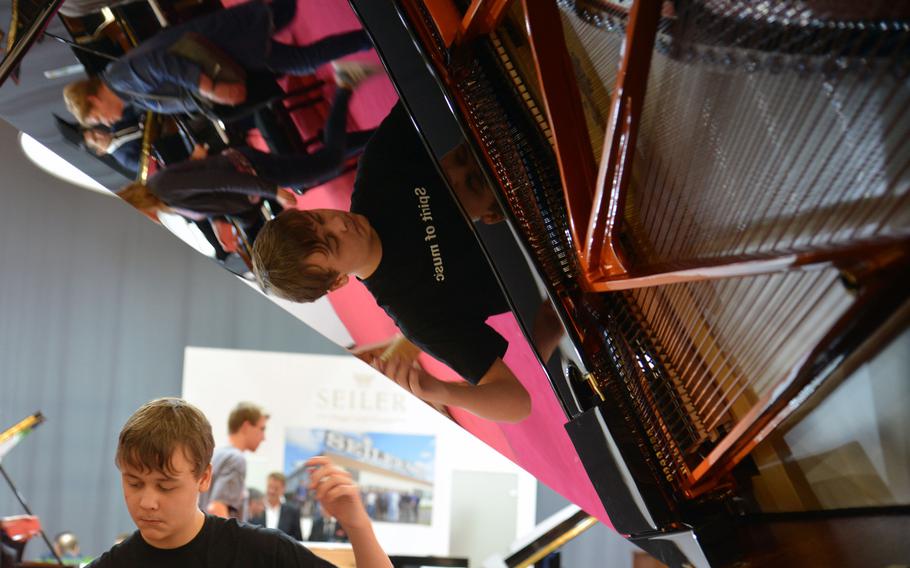 A young pianist is reflected in a shiny Schimmel grand piano as he plays at the Musikmesse in Frankfurt, Germany, Wednesday, April 11, 2018.