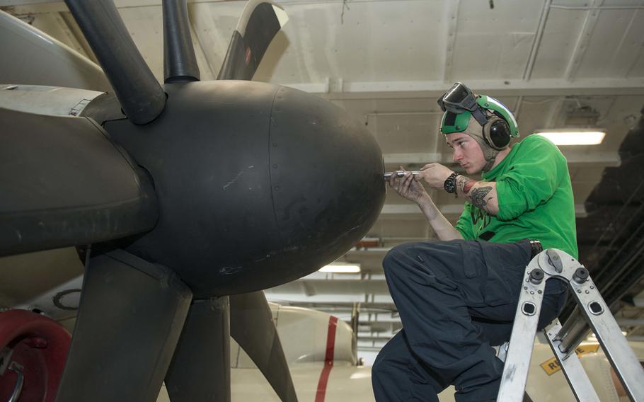 Petty Officer 3rd Class Justin Vennard, assigned to Carrier Airborne Early Warning Squadron 126, performs maintenance on an E-2D Hawkeye early warning and attack aircraft in the hangar bay of the USS Harry S. Truman, Saturday, April 14, 2018. The Truman and its carrier strike group have since entered the European theater of operations.