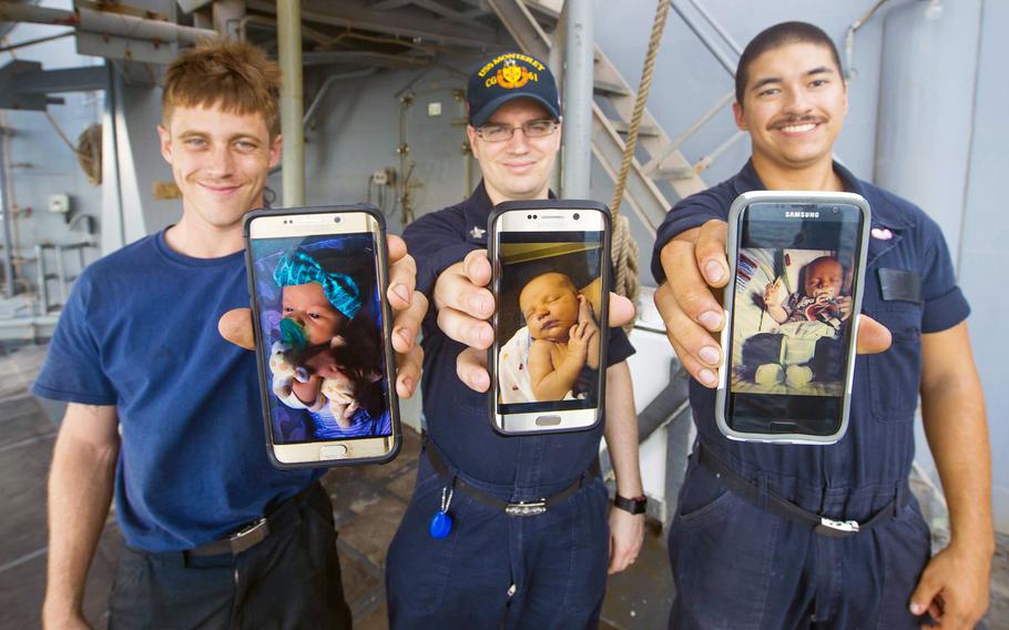 Seaman Cody Slone, left, Petty Officer 1st Class Joshua Morcom and Seaman Chase Marr show pictures of their newborn babies from their cellphones aboard the guided-missile cruiser USS Monterey. The Navy announced a new parental leave plan on Thursday.