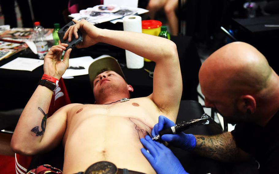Spc. Troy Meyer, a mechanic with the 64th Military Police Company, plays on his phone to distract himself as he gets a mountain scene tattooed on his ribs at the Grafenwoehr Tattoo Expo, in Grafenwoehr, Germany, Sunday, April 8, 2019.