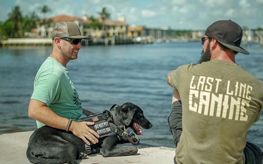 Greg Trost, left, is pictured here in Florida with his service dog Carmie and her trainer in an undated photo. Trost received Carmie through the charity Rebuilding Warriors in August 2018 to help him deal with the symptoms of a traumatic brain injury that resulted from a roadside bomb blast in Iraq in 2004. He and other Marines are raising money to donate a service dog to another Marine in need.
