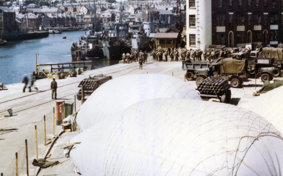 American troops load onto infantry landing ships at a port in Weymouth, England in June 1944, where barrage balloons have been anchored for protection against strafing and low level bombings.