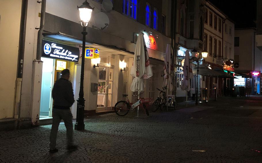 An individual walks by businesses in the pedestrian zone in Kaiserslautern, Germany at night. Maj. Gen. Christopher O. Mohan, commander of the Kaiserslautern-based 21st Theater Sustainment Command, on Monday, March 23, 2020 imposed a 10 p.m. to 5 a.m. curfew on soldiers, civilians, family members and contractors, as part of the effort to contain the coronavirus.