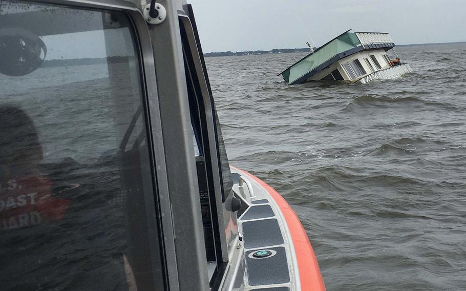 A boat from Coast Guard Station Elizabeth City, N.C., approaches a sinking houseboat on the Scuppernong River in Albemarle Sound, off North Carolina, June 13, 2020. Two people were hoisted from the vessel and a cat was transported to shore by the Coast Guard crew.