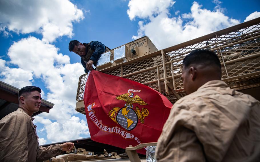 U.S. Marine Corps 1st Lt. Seth Gillen, left, Cpl. Jonathan Villanueva, middle, and Staff Sgt. Stephen Leon Guerrero, with 2nd Tank Battalion, 2nd Marine Division, hang a Marine Corps flag on the rear of an M1A1 Abrams tank on Camp Lejeune, N.C., July 27, 2020.