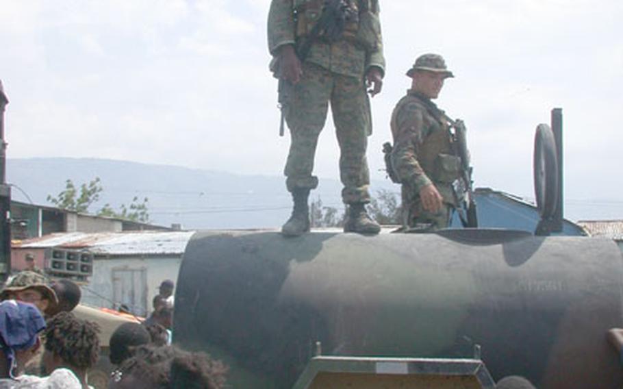 Marine Corps Cpl. Harry Milbin stands atop a water bull and tries to keep order of the crowd who gathered to fill their buckets with water provided by the Marines. The 28-year-old Haitian American, with India Company, 3rd Battalion, 8th Marines, said it&#39;s a dream-come-true to return to his native country wearing the uniform of a Marine.