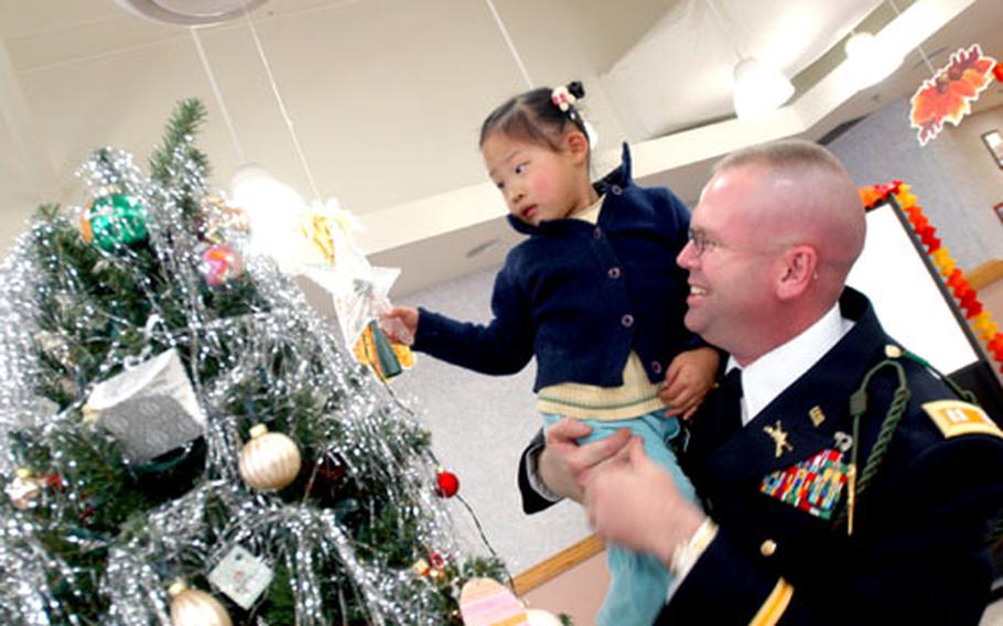 Capt. Dale Woodhouse, commander of Headquarters Headquarters Company, helps a little girl from the My Home Orphanage place a star on the Christmas tree.