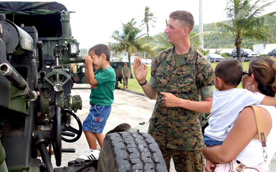 Pfc. Daniel O’Brien, of Kilo Battery 312, explains the workings of the unit’s M-198 medium towed howitzer to Guam resident Darla Flores as she holds son Tyler, 1, and her son Thaddeus, 4, looks through the weapon’s scope during Marine Day at Asan Beach Park, Guam, on Feb. 8.