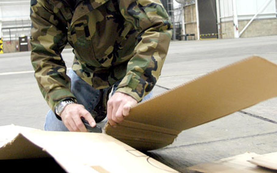 Air Force Master Sgt. Russell Carrington, of the 100th Maintenance Squadron, cuts cardboard that was being used to cover the drains inside Hangar 711 in preparation for the Yuletide Bazaar.