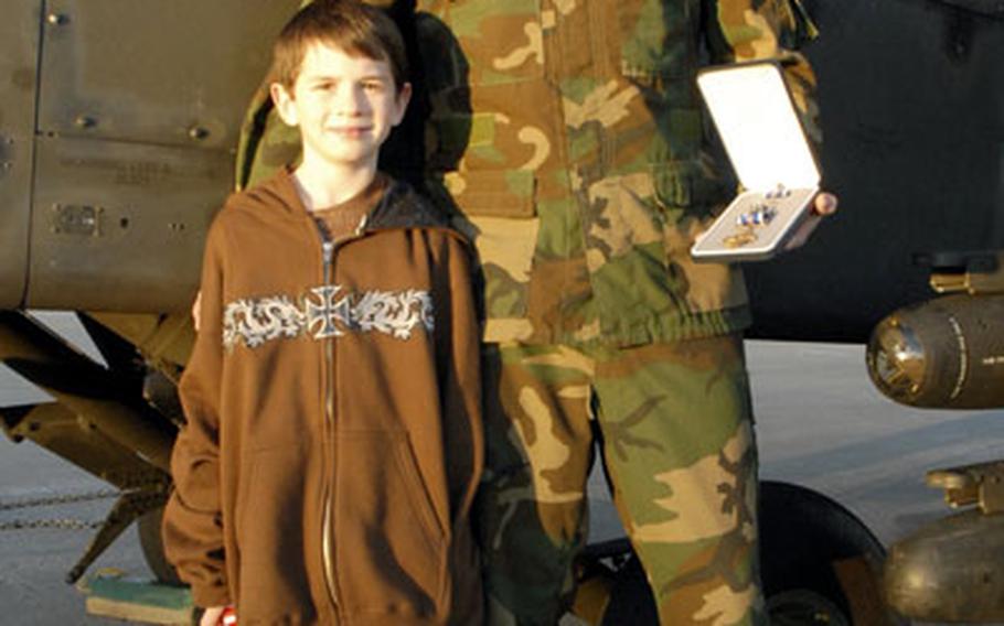 Chief Warrant Officer 2 Philip Learn, recipient of the Distinguished Flying Cross for aerial heroism last December in Afghanistan, stands with his 8-year-old son, Justin, next to an AH-64D Apache Longbow helicopter at Illesheim, Germany’s Storck Barracks on Friday. Learn is holding the award.