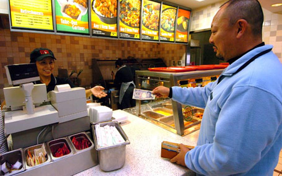 Nao Aoki, right, uses yen rather than U.S. dollars to pay for his food Dec. 24 at the Main Street Food Court on Yokosuka Naval Base, Japan.