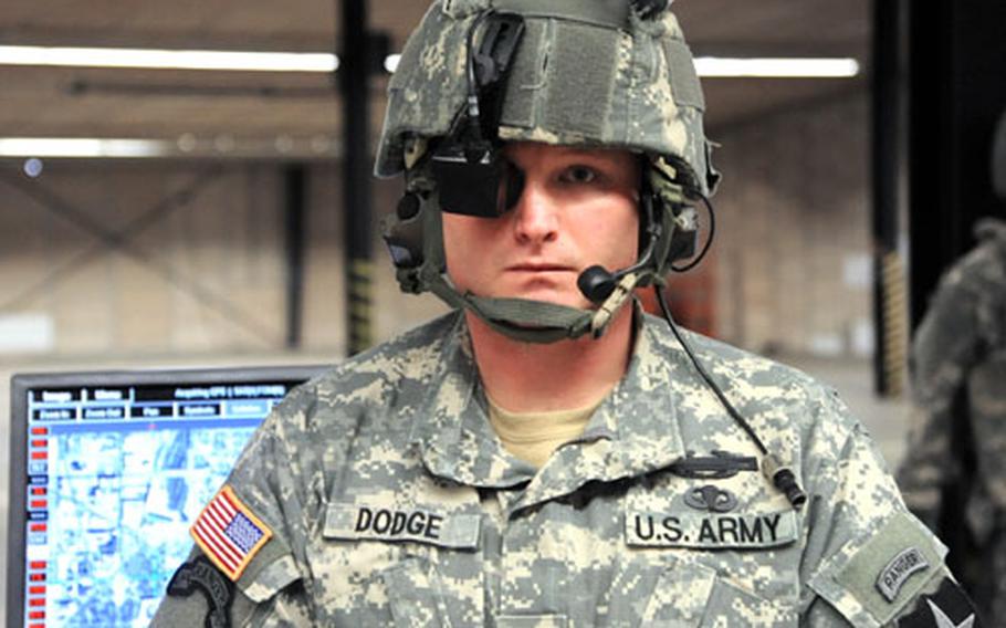 At a military technology expo in Kaiserslautern, Germany, Staff Sgt. Matt Dodge wears a helmet with a mounted display and earphones that are part of the Land Warrior system. Dodge used the system, when he was deployed to Iraq with 4th Battalion, 9th Infantry Regiment, 4th Brigade Combat Team, 2nd Infantry Division. It links dismounted soldiers with the digital battlefield network. Dodge can see the image that&#39;s on the large screen behind him using his mounted display.