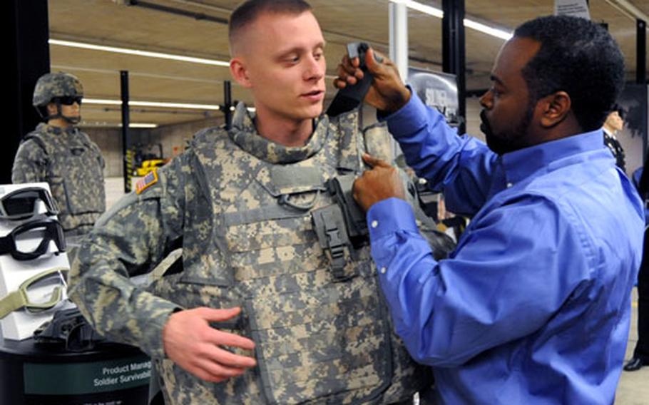 Francis Hayden, right, director of operations for Product Manager Soldier Survivability, straps an Improved Outer Tactical Vest on Spc. Dorian Thomas at a military tech expo in Kaiserslautern, Germany on Monday. Soldiers can instantly remove the vest in emergency situations by pulling the release handle at its center.