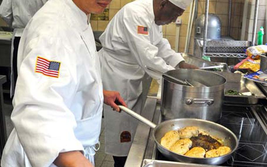 Daniel Trawick, left, fries chicken breasts stuffed with goat cheese and spinach , while Julian Gude prepares green beans wrapped in smoked ham, in the Keyes Building kitchen on Campbell Barracks in Heidelberg, Germany.