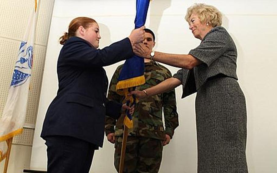 Diana Ohman, director of Department of Defense Dependents Schools-Pacific, passes the Air Force Junior ROTC guidon over to Cadet Maj. Chelsea Northcutt, a senior at Yokota High School, during a ceremony recognizing them as an Air Force Junior ROTC unit.