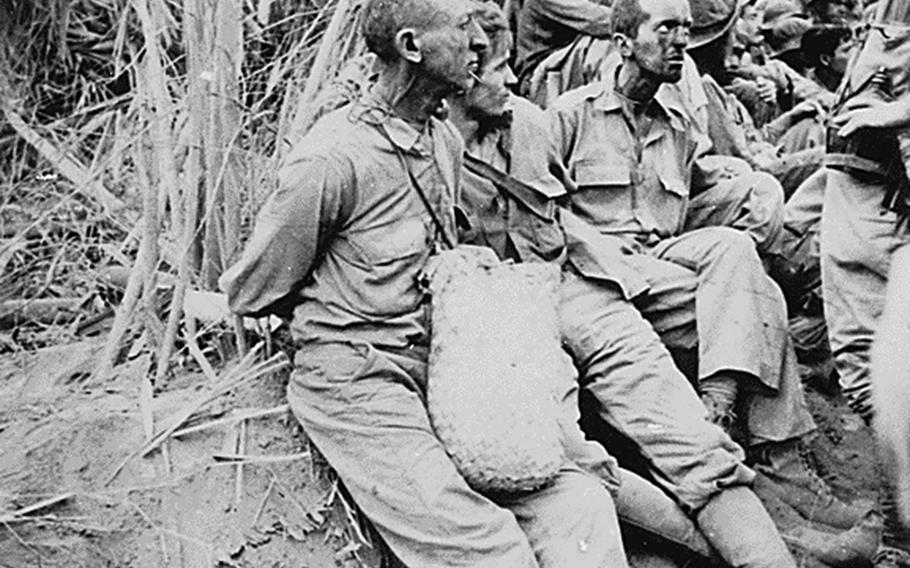 American prisoners of war pause along the Bataan Death March on their way to Cabanatuan prison camp with their hands behind their backs in April or May 1942. 