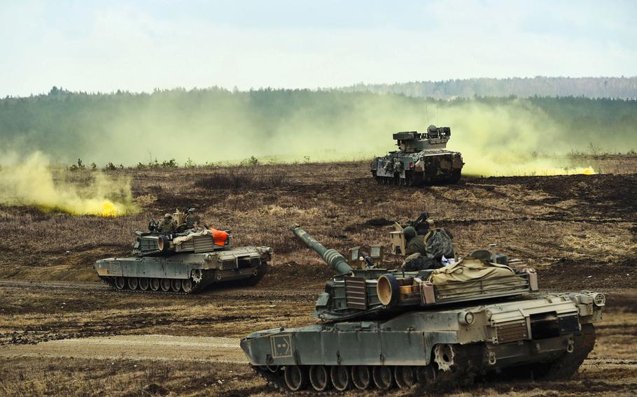 M1A2 Abrams tanks and Bradley Fighting Vehicles converge on a smoke signal during a live-fire exercise at Grafenwoehr, Germany, in March. President Trump is pushing a plan that demands allies pick up the full cost of hosting U.S. troops in their countries, plus a 50 percent premium for American protection, according to a news report.