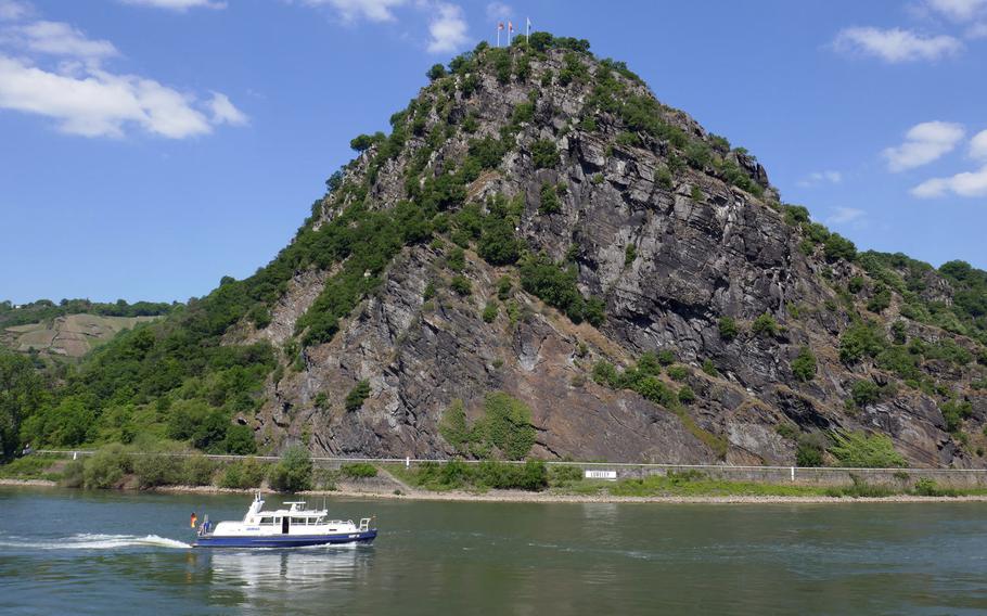 A boat travels up the Rhine River, past the Lorelei, a rock jutting 410 feet above the river. Just a bit upriver, where it makes a slight curve, is the narrowest and deepest point of the river. On top of the rock is the main viewing platform with its flags.