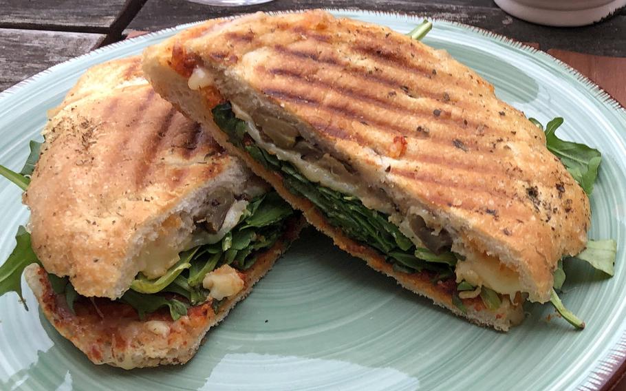 A takeout focaccia Sicilia from Vinocentral in Darmstadt, Germany. It includes olive tapenade, grilled, marinated vegetables and Provolone cheese on a bed of arugula.