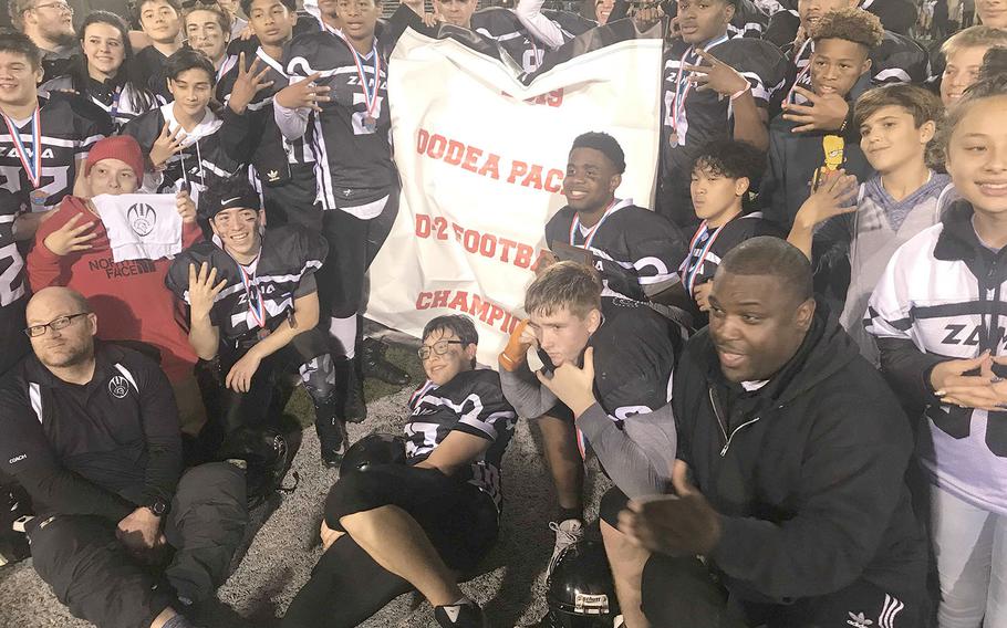 Zama players and coaches gather round the banner. It's the third Far East Division II football title in school history.