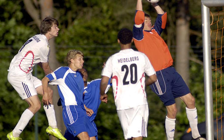 Taylor Shepard of Ramstein stops a shot as Kevin Beerman of Heidelberg leaps over the back of Jonathan McLouth during the DODDS Division I soccer championship game Friday at Ramstein High School. Shepard dropped the ball, causing Heidelberg players to scramble for another shot; Enrique Grandacarpio was ejected from the game for contact with the goalie. Ramstein won in overtime, 1-0.