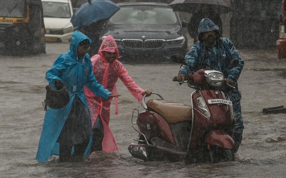 Children push their father's scooter through a flooded street as it rains in Mumbai, India, on July 25, 2024. 