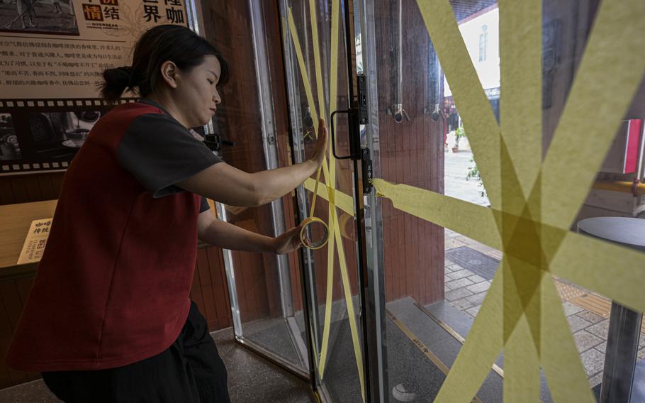 In this image released by Xinhua News Agency, a worker reinforces a glass window with tape at a cafe after the State Flood Control and Drought Relief Headquarters raised its emergency response for flood and typhoon prevention for Typhoon Yagi, Thursday, Sept. 5, 2024, in Haikou, south China's Hainan Province. 