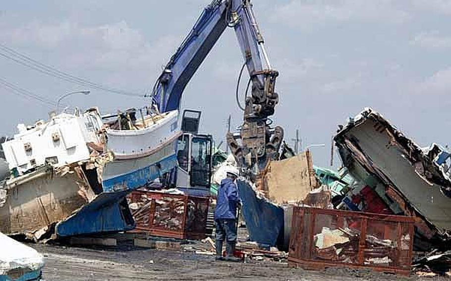 Japanese workers use heavy machinery Tuesday at the Misawa City port to smash apart boats that were washed ashore in a March 11 tsunami. Officials are trying to get the port ready for a mid-June squid harvest, which is vital to the local economy.