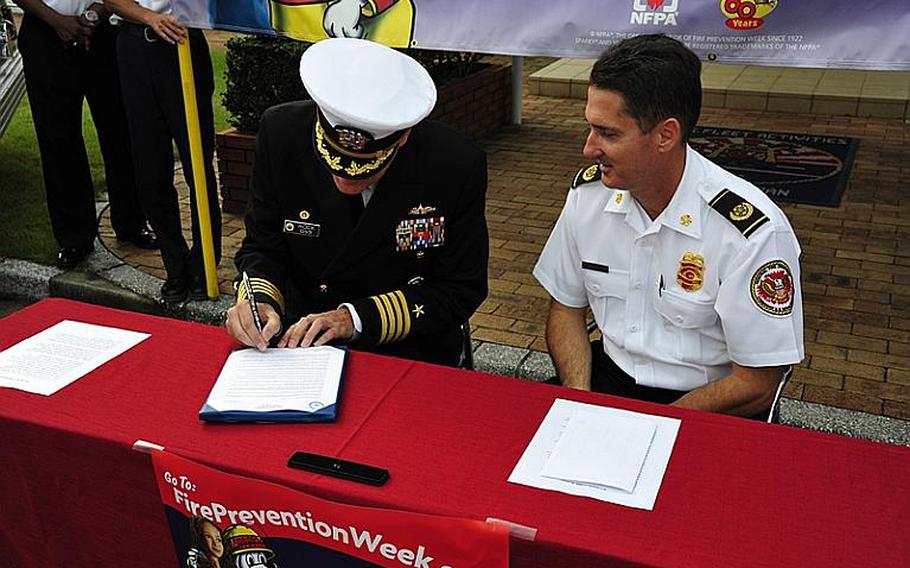 Commander Fleet Activities Sasebo Capt. Charles Rock, left, sits with Installation Fire Chief Gerald Clark and signs a proclamation Tuesday morning in front of the captain's office to declare Oct. 9-15 Fire Prevention Week at the base. In addition to fire drills and raising awareness with children on the base, the Sasebo department also does outreach with local Japanese school children. Fire Prevention Week is being observed nationwide this week in the U.S. and in DODEA schools around the globe.