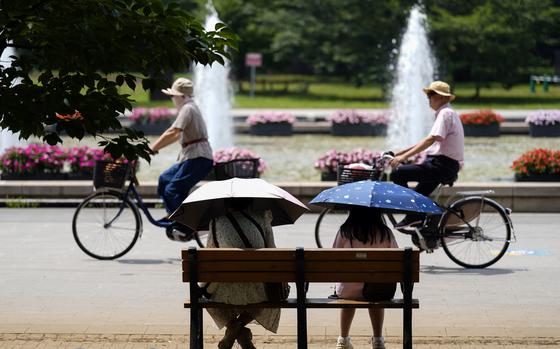 People holding parasols sit on the bench under an intense sun at a park in Tokyo, July 8, 2024. Japan’s total population marked the 15th straight year of decline, according to government data released Wednesday, July 24. 