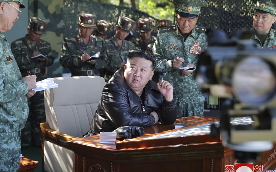 Kim Jong Un sits at a desk and speaks with military personnel.