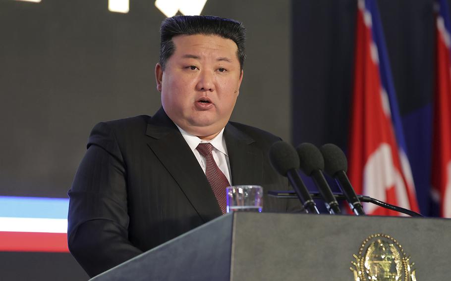 Kim Jong Un delivers a speech while standing at a podium in front of North Korean flags.