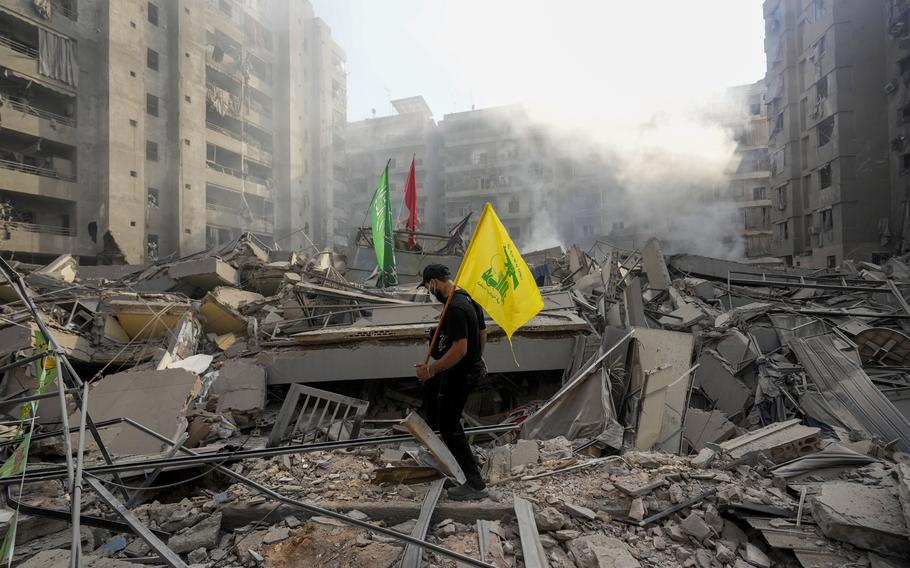 A man carries a flag through the rubble of an apartment building.