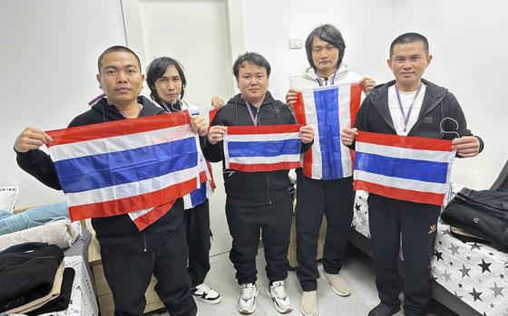 Five men stand in a hospital room holding Thailand flags.