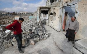 Two men stand amidst rubble in Syria.