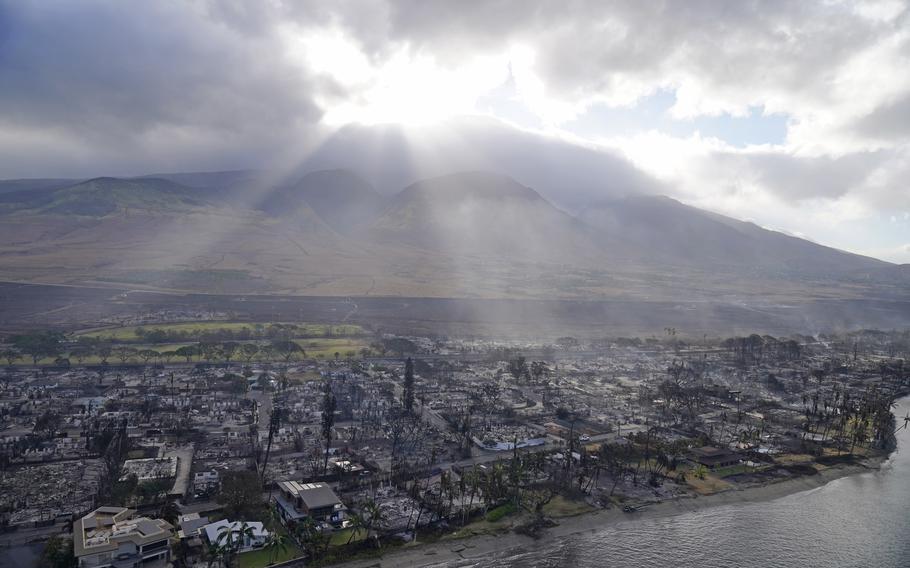 Rays of sunlight pierce through the clouds, Thursday, Aug. 10, 2023, above homes burned by wildfires in Lahaina, Hawaii. 