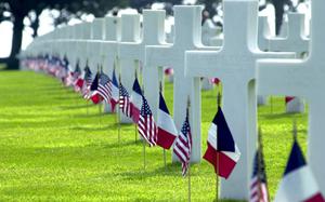 Rows of crosses and Stars of David stand in long rows at Normandy American Cemetery, Colleville-sur-Mer, France, decorated with American and French flags. The cemetery is the final resting place for 9,386 of our war dead. 