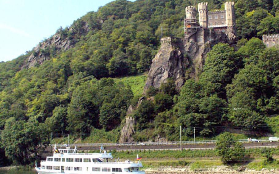 A cruise boat passes what remains of the Rheinstein castle, sitting on a rocky ledge above the Rhine River. Tourists out to admire castles have to do what invaders in the Middle Ages did — look up.